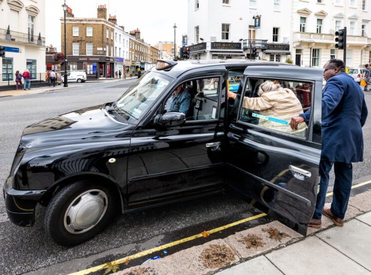 London, UK - September 12, 2018: Pimlico or Victoria street road with historic architecture and man helping woman get into black taxi cab