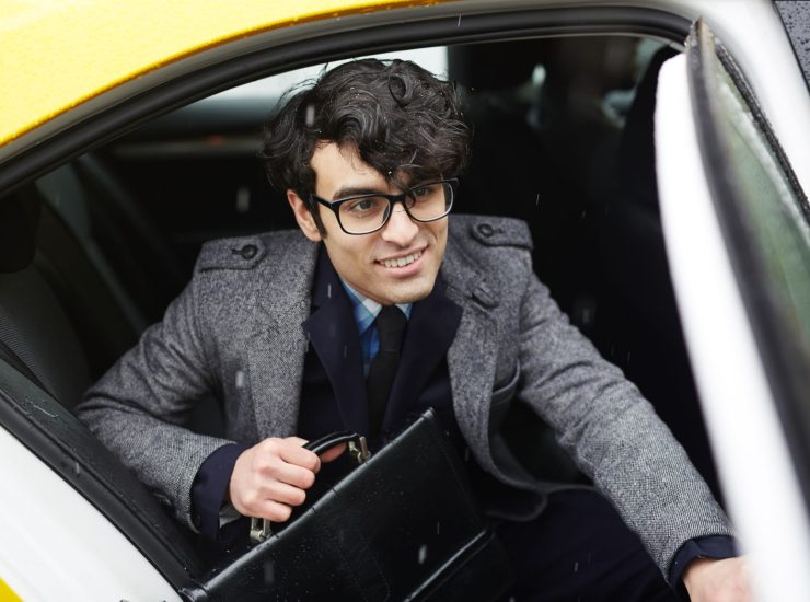 Portrait of young smiling  Middle-Eastern businessman with briefcase getting out of taxi to rainy autumn street